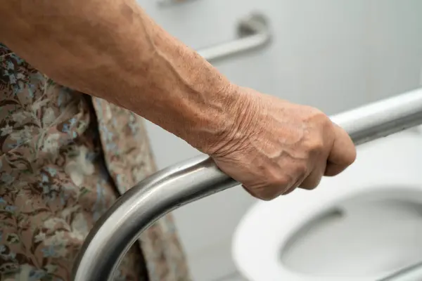Asyalı yaşlı kadın hasta tuvalette tuvalet desteği kullanıyor..