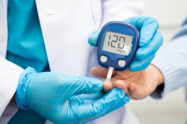 Diyabet tedavisinde kan şekeri seviyesini kontrol etmek için dijital glikoz ölçer kullanan Asyalı doktor.