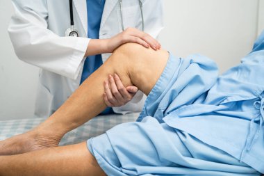 Doktor, hastanede dizinde yara izi olan Asyalı yaşlı kadın hastayı kontrol ediyor..