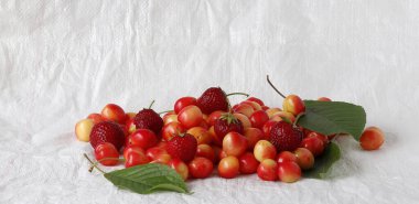 Olgun pembe kirazlar ve olgun çilekler beyaz bir arka planda yatıyor..