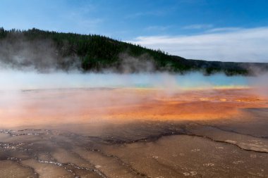 Yellowstone kaplıcaları buharlı ve rengarenk arka planda dağlar var.