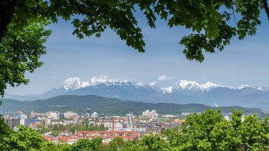 Ljubljana 'nın arka planda tepeleri ve yapraklarla çerçevelenmiş Alp dağları manzarası