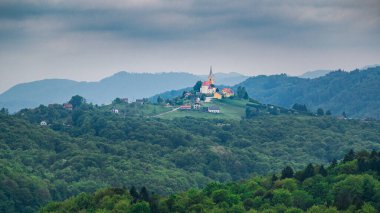 Slovenya 'nın dağlarındaki küçük bir köyün güzel manzarası tepenin üstündeki kilise.