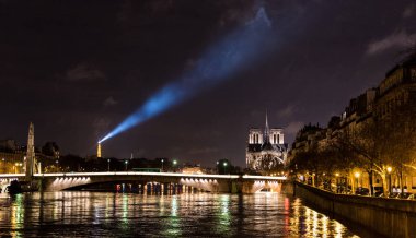 Sağda Notre Dame de Paris ile Seine nehri ve solda Eyfel Kulesi ve ışık hüzmesi.