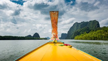 Tayland 'da bir körfezde yelken açan sarı bir Tayland teknesinin önünde.