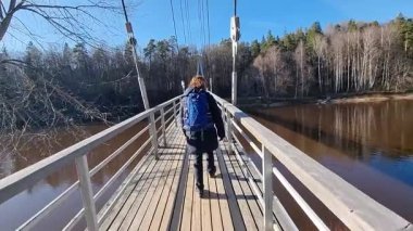 Sırt çantalı bir kadın Gauja nehri üzerindeki yaya köprüsünden geçiyor. Yüksek kalite 4k görüntü