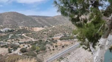 Kıbrıs 'ta, tepeler ve Akdeniz bitkileriyle çevrili vadiden geçen eğimli bir yolu olan manzaralı bir dağ manzarası. Görüntüler sakin kırsal güzelliği ve dolambaçlı yolları yakalıyor.