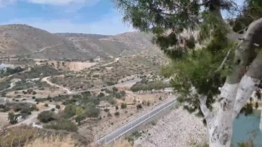 Kıbrıs 'ta, tepeler ve Akdeniz bitkileriyle çevrili vadiden geçen eğimli bir yolu olan manzaralı bir dağ manzarası. Görüntüler sakin kırsal güzelliği ve dolambaçlı yolları yakalıyor.