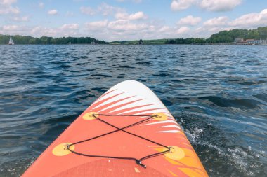 Üzerinde sarı bir güneş olan bir sörf tahtası suyun üzerinde yüzüyor. Su sakin ve gökyüzü berrak.
