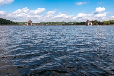 Su sakin ve gökyüzü mavi. Kıyıda iki küçük ev var. Su derin ve gökyüzü berrak.