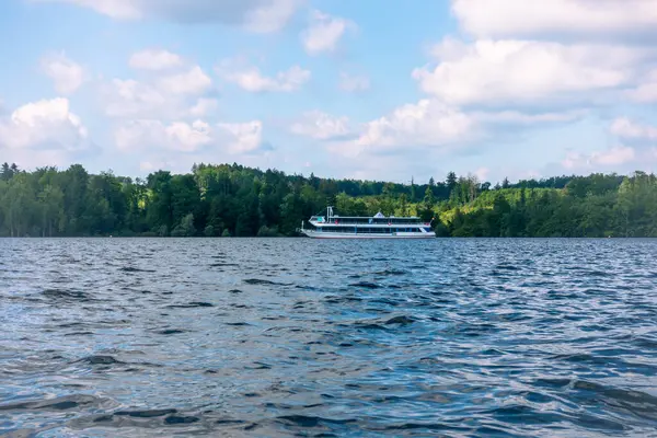 Arka planda açık mavi gökyüzü olan bir gölde büyük bir tekne seyrediyor. Sahne huzurlu ve sakin. Tekne suda görünen tek nesne.