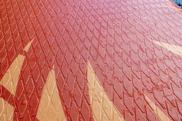 Üçgen desenli kırmızı ve kahverengi bir yüzey. Yüzey ıslak ve parlak görünüyor.