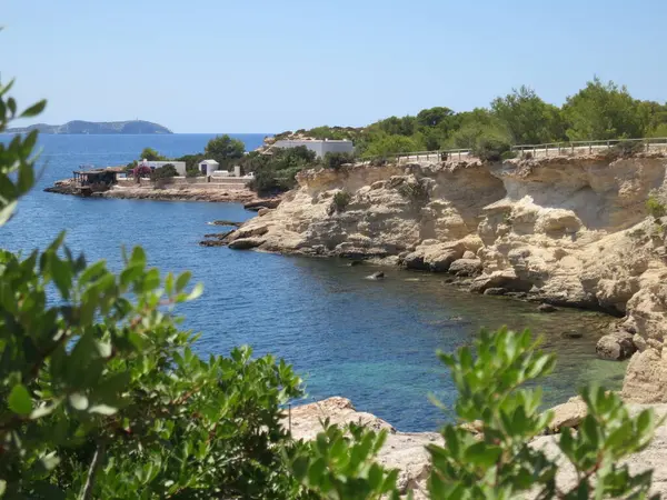 Arkasında kayalık bir uçurum olan güzel bir sahil. Su sakin ve berrak. Huzurlu ve huzurlu bir sahne.