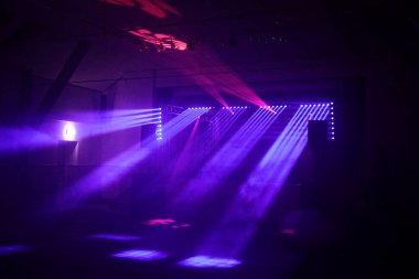 Mor ışıkları ve spot ışıkları olan karanlık bir oda. Sahne gizemli ve dramatik.