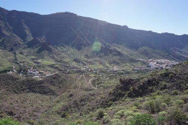 Vadide küçük bir kasabası olan bir dağ sırası. Kasaba ağaçlarla çevrilidir ve dağlar yeşil bitki örtüsüyle kaplıdır. Gökyüzü açık ve güneş parlıyor.
