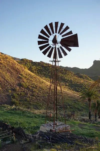 Bir yel değirmeni, dağların güzel manzaralı bir tarlada duruyor. Yel değirmeni eski ve paslı, ama hala uzun ve gururlu duruyor. Huzurlu ve huzurlu bir sahne.