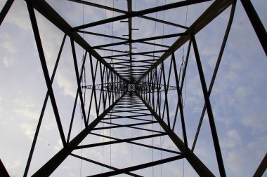 Arka planda açık mavi gökyüzü olan uzun metal bir yapı. Bina uzun ve bir sürü kablosu var.