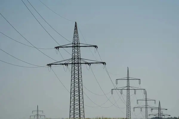 Gökyüzünde bir dizi uzun elektrik hattı görülüyor. Elektrik hatları siyah beyaz ve bir elektrik santraline bağlı.