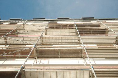 Üzerinde iskele olan bir bina. İskele mavi ve kırmızı renktedir. Bina yüksek.