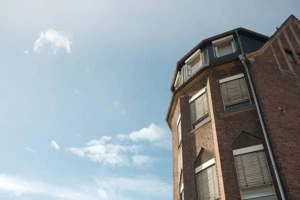 Arka planda mavi gökyüzü olan tuğla bir bina. Binanın bir sürü penceresi ve eğimli bir çatısı var.