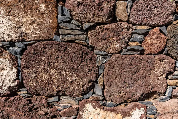 Kahverengimsi renkte taşlardan yapılmış bir duvar. Duvar küçük kayalardan yapılmış ve pürüzlü bir dokusu var.