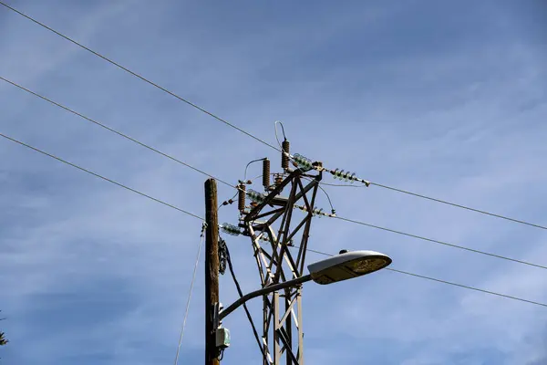 Tepesinde sokak lambası olan uzun bir elektrik direği. Gökyüzü açık ve mavi. Direk elektrik hatlarıyla çevrili.