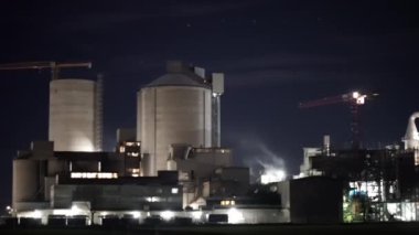İki uzun silosu olan büyük bir sanayi tesisi gece aydınlandı. Sahne endüstriyel ve biraz da uğursuz.