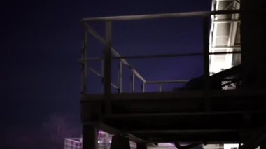 Arka planda karanlık bir gökyüzü olan bir köprüde korkuluk. Korkuluklar aydınlanıyor, karamsar bir atmosfer yaratıyor.