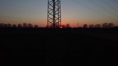 Üzerinde elektrik hattı olan uzun bir direk. Gökyüzü turuncu ve güneş batıyor.