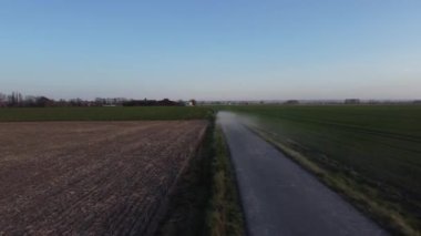 Önünde açık mavi bir gökyüzü olan uçsuz bucaksız, boş bir araziden geçen bir yol. Yol büyük oranda boş, görünürde araba ya da diğer araçlar yok. Gökyüzü berrak ve bulutsuz