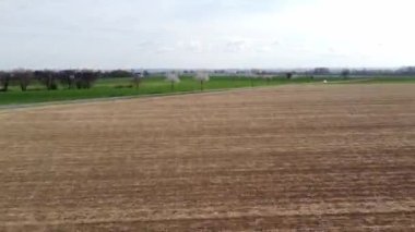 Arka planda ağaç olmayan bir toprak tarlası. Gökyüzü bulutlu ve güneş görünmüyor.