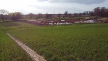 İçinden toprak yol geçen bir çim tarlası. Gökyüzü bulutlu ve güneş parlıyor