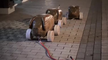 Üç ahşap oyuncak araba bir tuğla kaldırıma zincirlenir. Arabalar kahverengi ve tekerlekleri var.