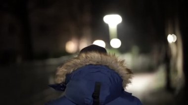 Kapüşonlu mavi ceket giyen biri karanlık bir sokakta yürüyor. Karmaşık ve gizemli bir görüntüsü var. Karanlıkta tek başına yürüyen kişi gibi.