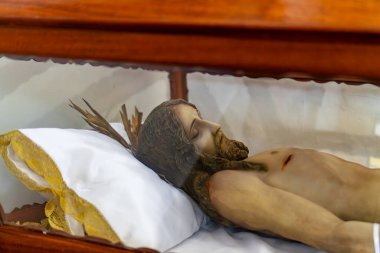 Bir adamın bedeni, altında beyaz bir yastıkla cam bir kutuda sergilenir. Adamın kafası yastığın üzerinde dinleniyor ve vücudu rahat bir pozisyonda yatıyor.