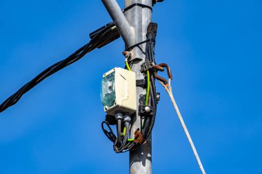 Üzerinde kutu olan ve içinden kablolar çıkan bir direk. Kutu beyaz ve üzerinde yeşil ışık var.