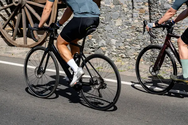 İki kişi bir yolda bisiklet sürüyorlar. Motosikletlerden biri siyah, diğeri kırmızı.