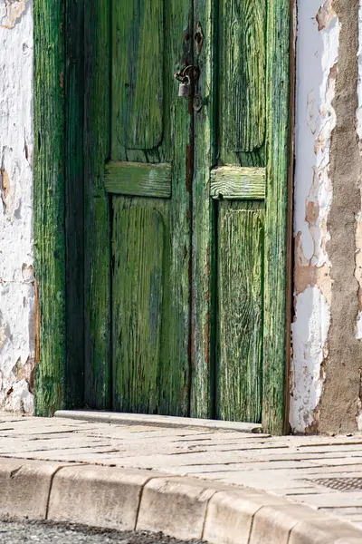 Ahşap çerçeveli yeşil bir kapı açık. Kapı beyaz bir duvarın önünde.