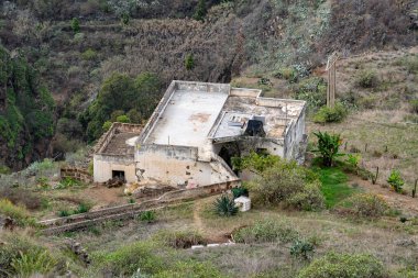 Çatısı olan bir ev yukarıdan görülür. Çatı kiremitleri kayıp ve ev bakımsız görünüyor.