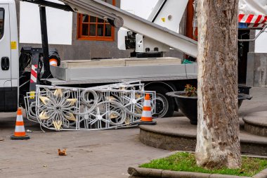 Bir ağacın önüne park edilmiş bir kamyon var. Kamyon büyük bir ekipman taşıyor.