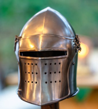 Bir ortaçağ miğferi arka planda bulanıklaşır, karmaşık tasarımı ve tarihsel önemi gözler önüne serilir.