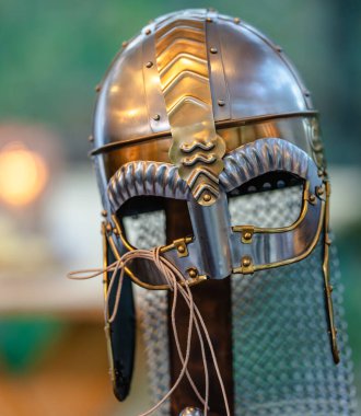 Bir ortaçağ miğferi arka planda bulanıklaşır, karmaşık tasarımı ve tarihsel önemi gözler önüne serilir.