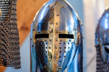 Bir ortaçağ miğferi arka planda bulanıklaşır, karmaşık tasarımı ve tarihsel önemi gözler önüne serilir.