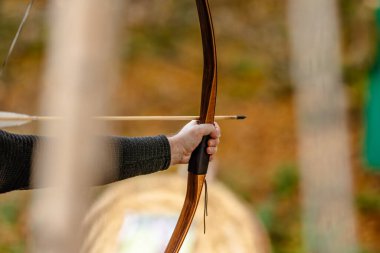 Elinde yay ve ok olan bir adam ormanda bir hedefi vurmaya hazırlanıyor.