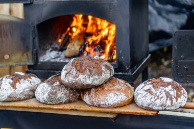 Taze pişmiş ekmek, ahşap raflarda altın somunlar ve arka planda parlayan bir ateş sıcak bir ortam yaratıyor..