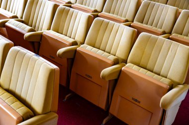 Tiyatroda bir sıra sandalye boş. Sandalyelerin hepsi aynı renkte ve sıra sıra dizilmiş.