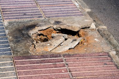 Kaldırımda bir delik ve yanında da tuğla bir duvar. Çukur toprak ve molozlarla dolu.