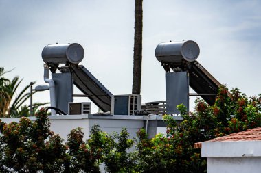 İki güneş paneli bir çatıya monte edilir, biri solda ve biri sağda. Arka planda bir palmiye ağacı görülebilir ve sahneye doğanın bir dokunuşunu ekler. Sahne sakin ve sakin.