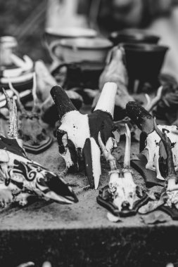 Kafatası ve kemiklerle dolu bir masa, bazıları boyanmış. Kafatasları çeşitli pozisyonlarda sıralanır, bazıları ön planda, diğerleri arka planda yer alır.