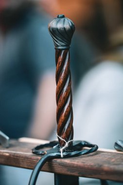 A wooden sword with a black tip and a silver ring is sitting on a wooden table. The sword has a unique design and he is quite old clipart